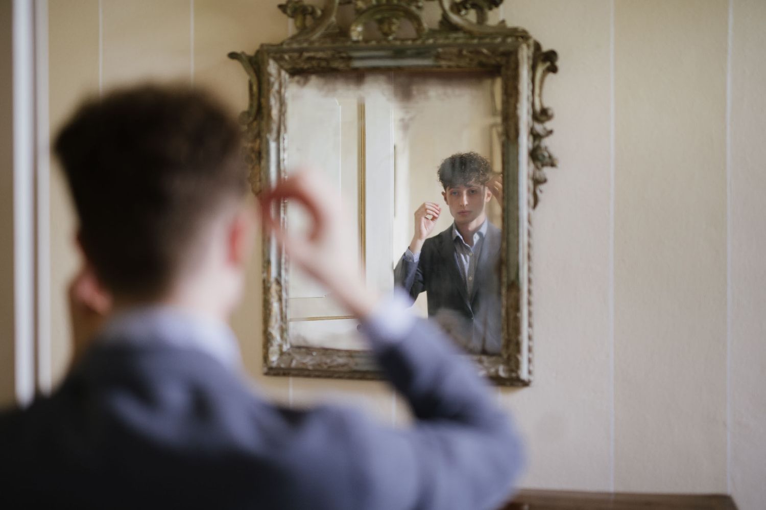 Reflection in ornate vintage mirror showing someone adjusting formal attire.