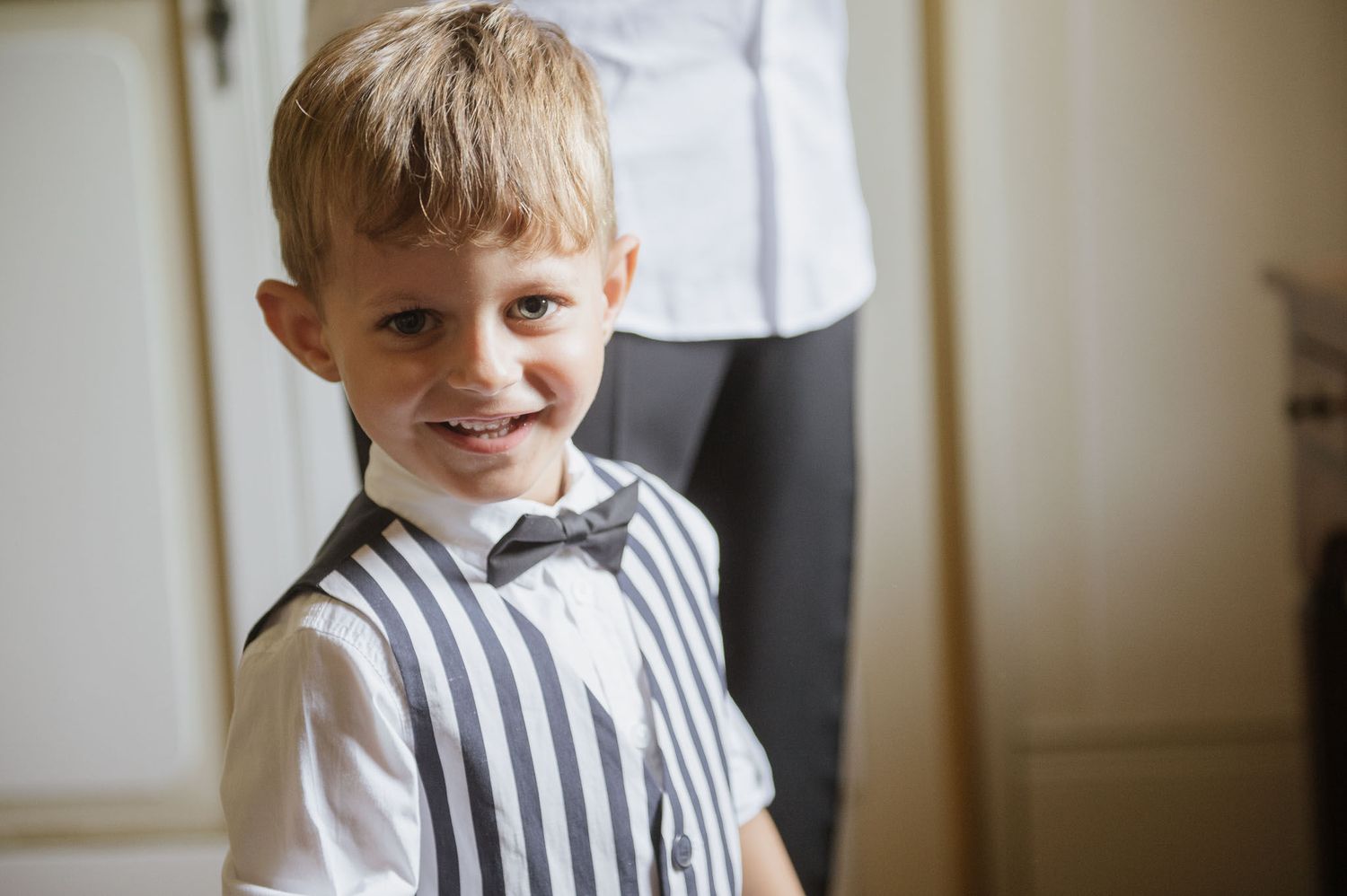 Young boy in a striped shirt and bow tie smiles warmly at the camera.
