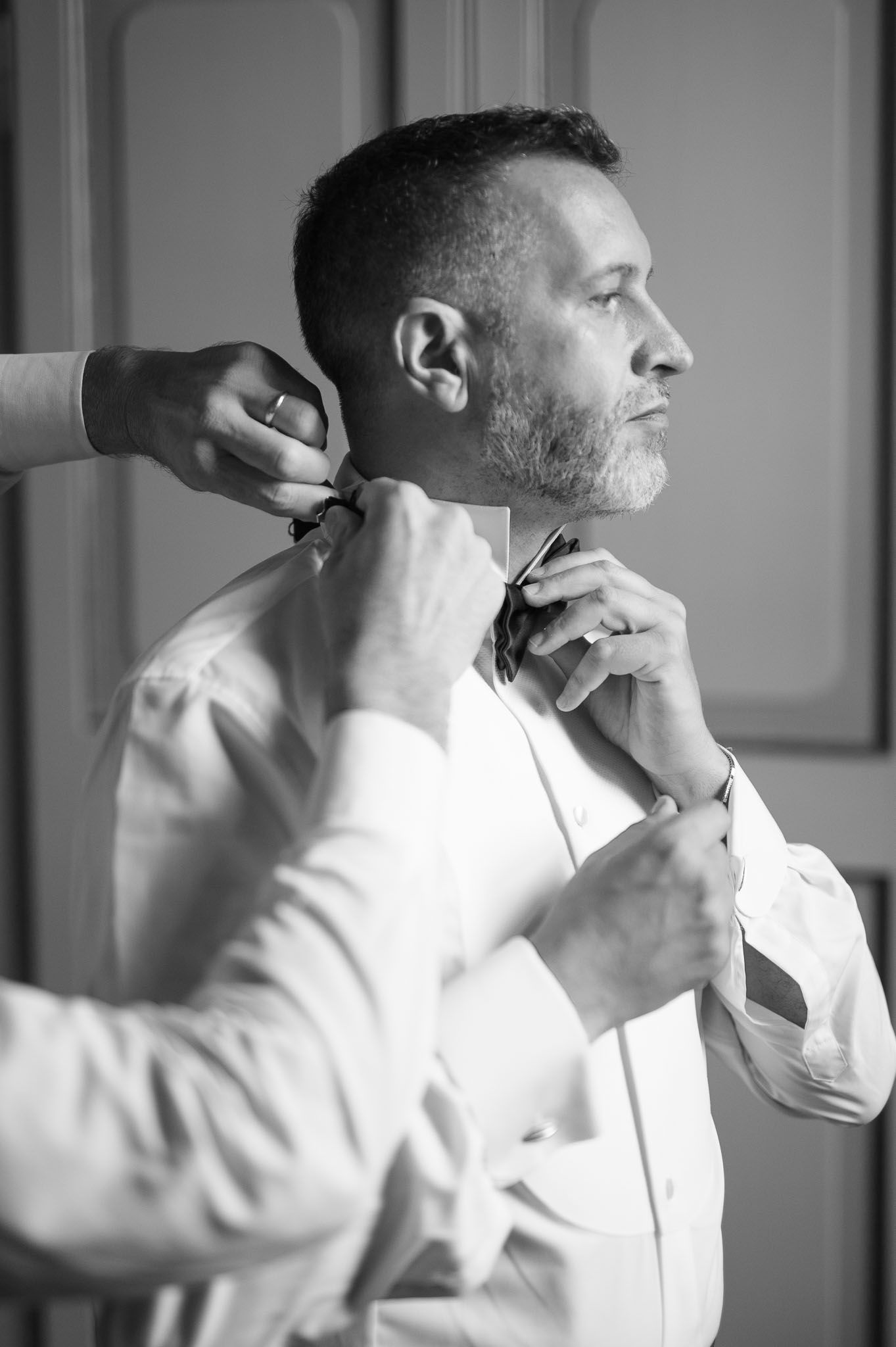 Hands adjusting a bow tie on a man in white dress shirt during formal preparation.
