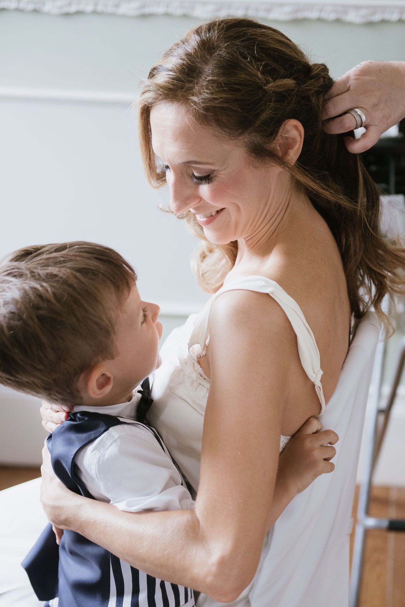 Woman in white dress sharing tender moment with young child in formal attire.
