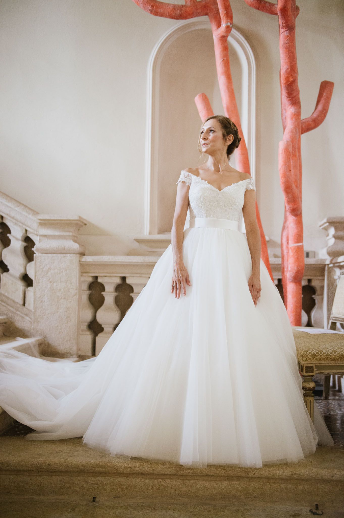 Bride in off-shoulder wedding dress poses near unique coral-colored sculptural elements.