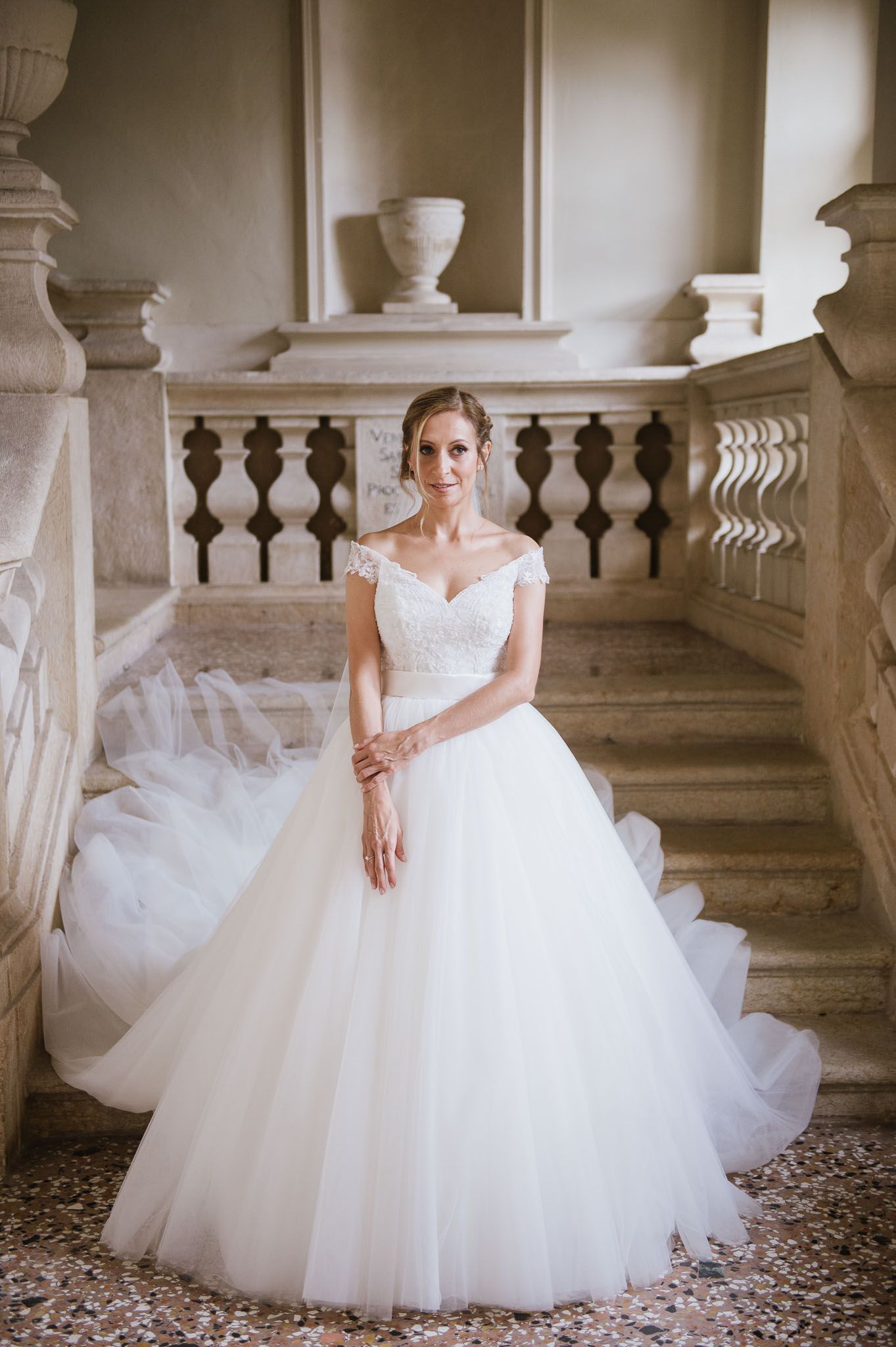 Bride in classic tulle ballgown poses on ornate stone staircase.
