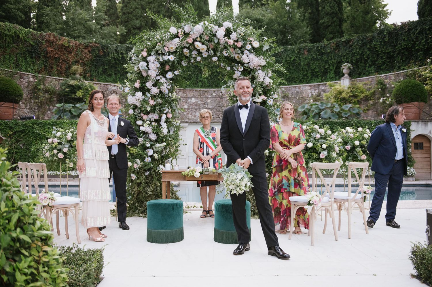 Garden wedding ceremony setup with floral arch and guests gathered under romantic lighting.