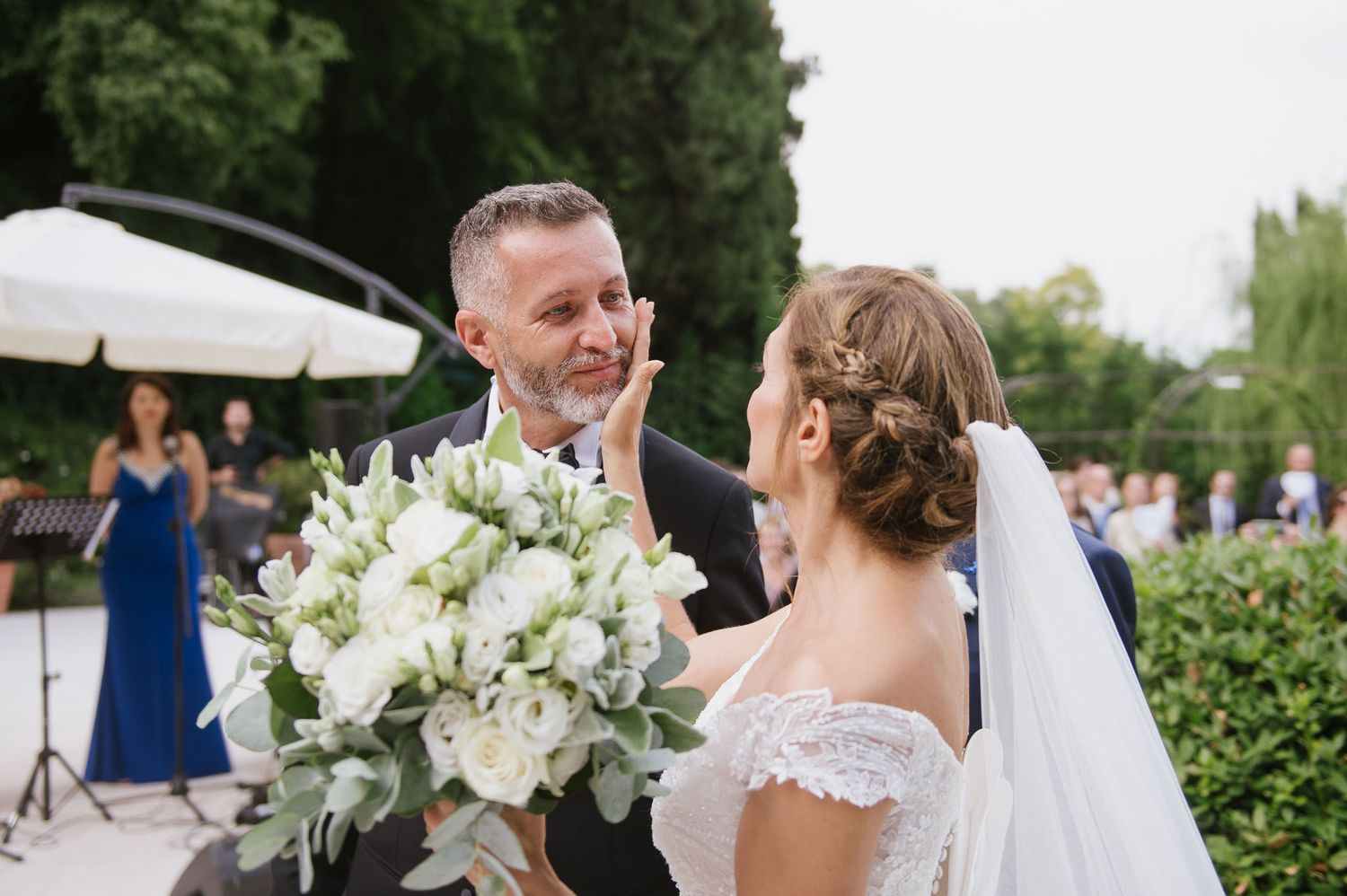 Outdoor wedding celebration with white floral bouquet against garden backdrop.