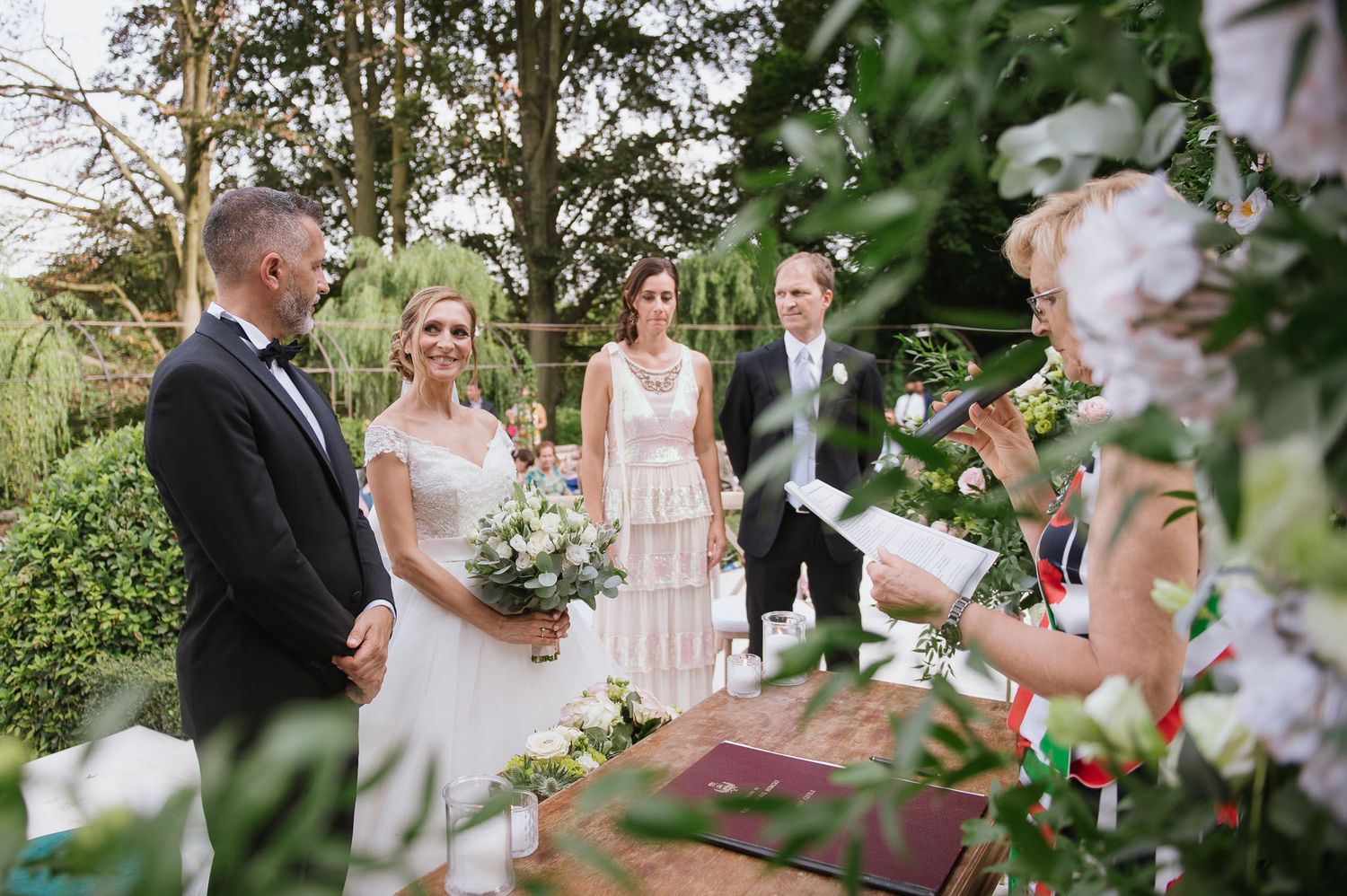An intimate outdoor wedding ceremony takes place in a garden setting with elegant decorations and floral arrangements.