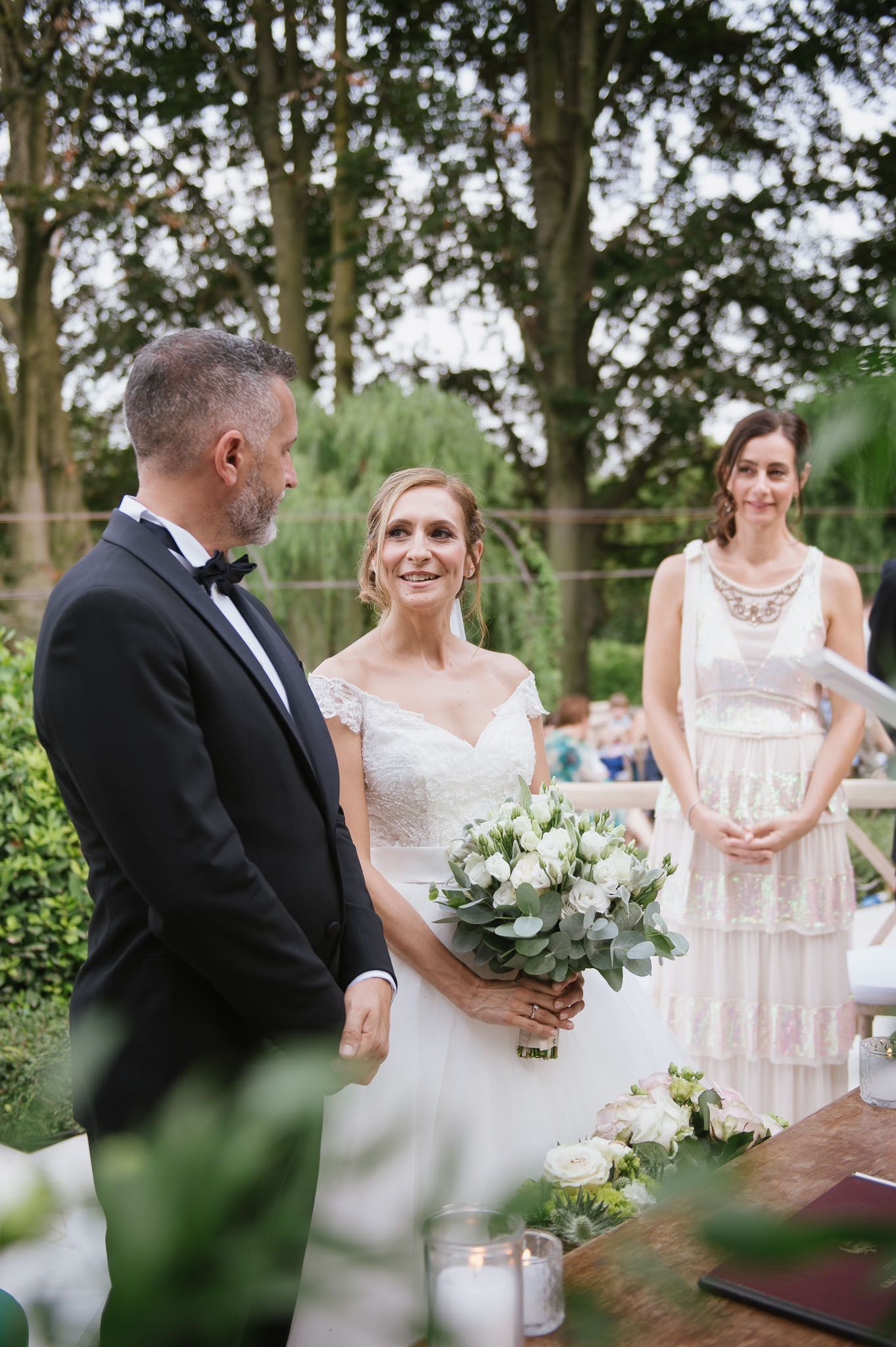 An intimate garden wedding ceremony with white floral bouquets and elegant formal attire.