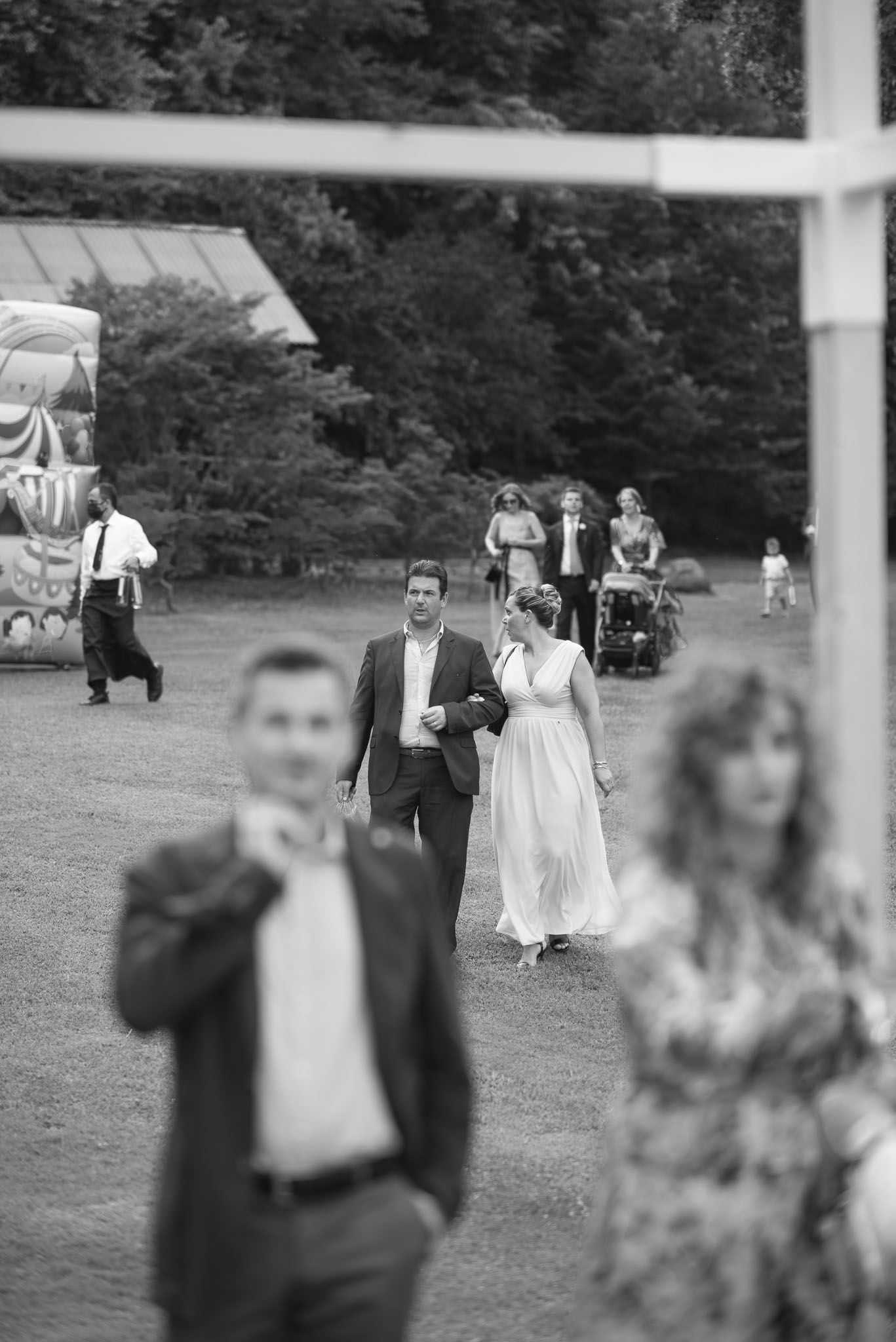 Black and white candid photo of wedding guests mingling outdoors during a garden reception celebration.