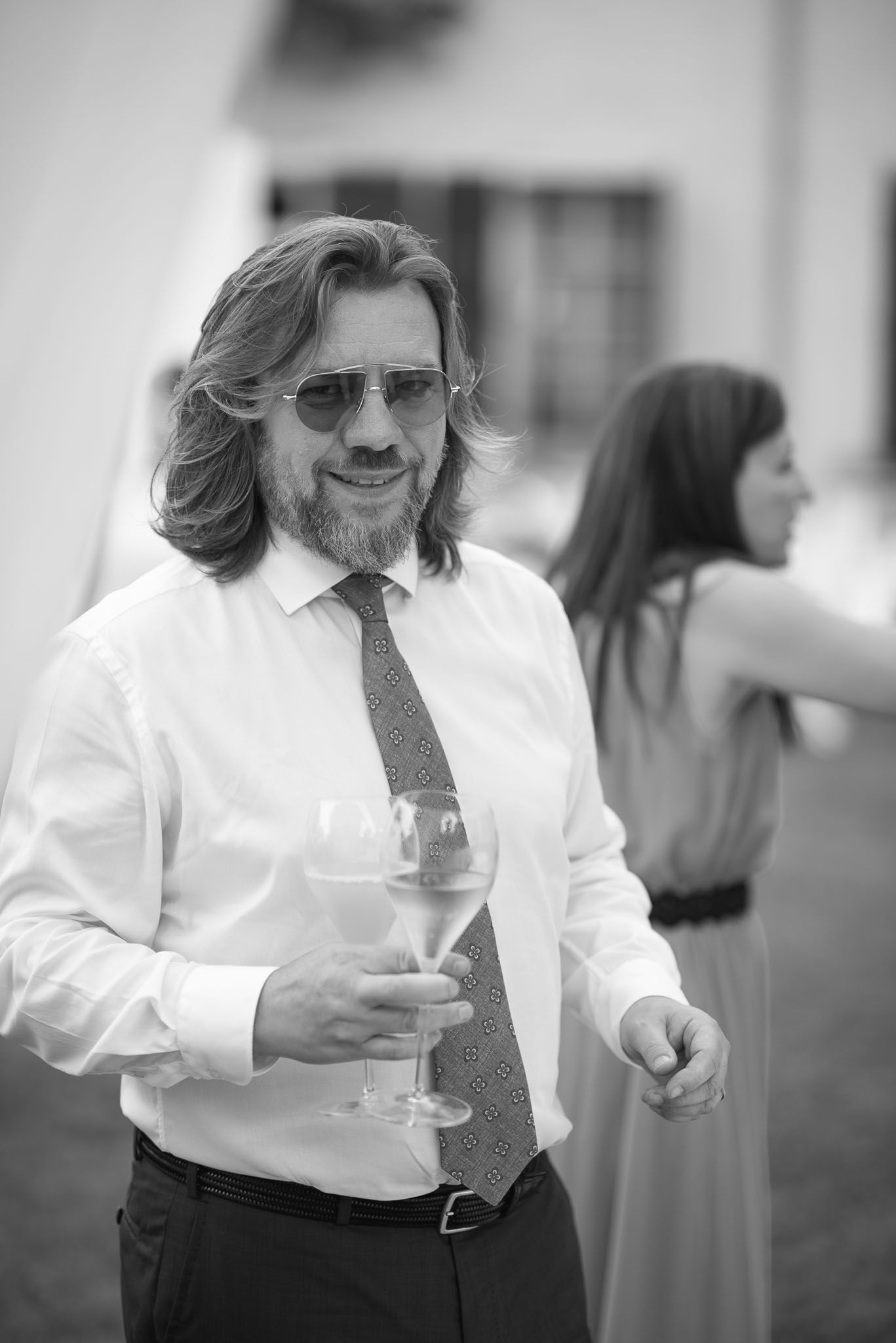 Wedding guest in formal attire holding wine glass at outdoor reception.