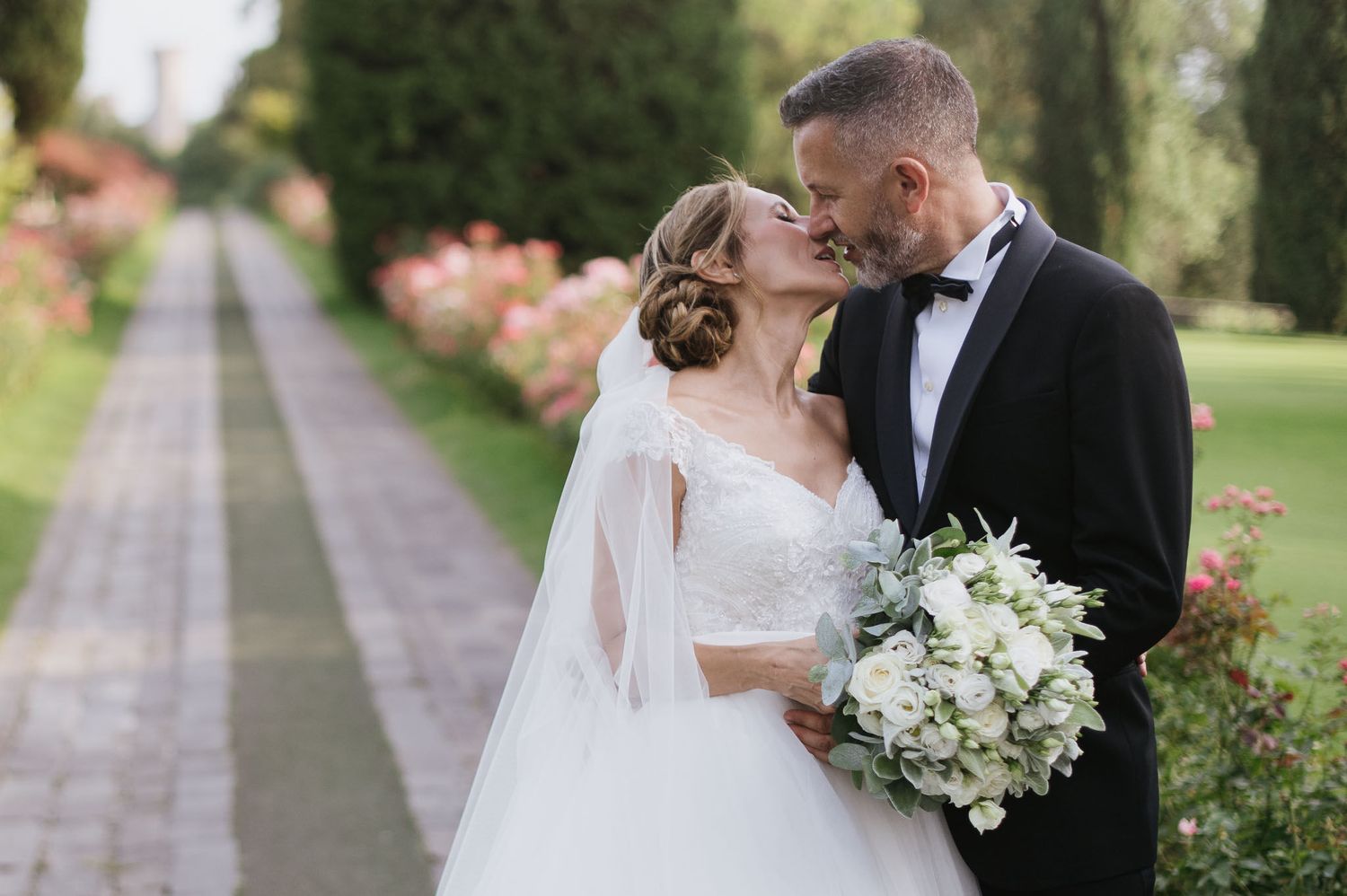 Romantic wedding couple sharing a moment on a garden path surrounded by blooming flowers.