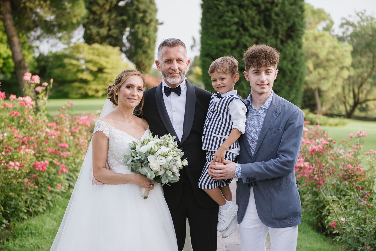 Wedding group portrait in a beautiful rose garden with formal attire.