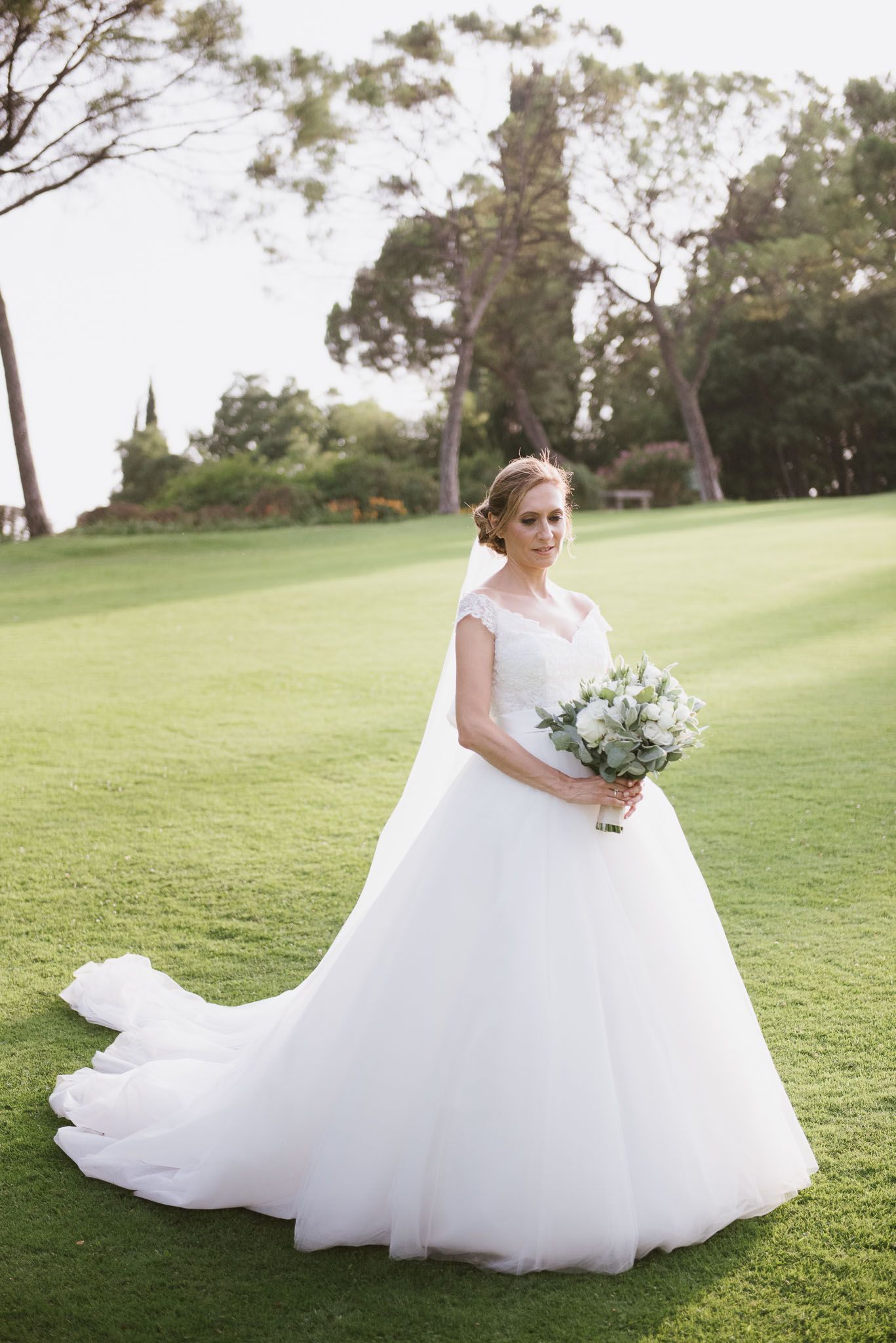 Stunning bride in princess ballgown poses on manicured golf course with flowing train.