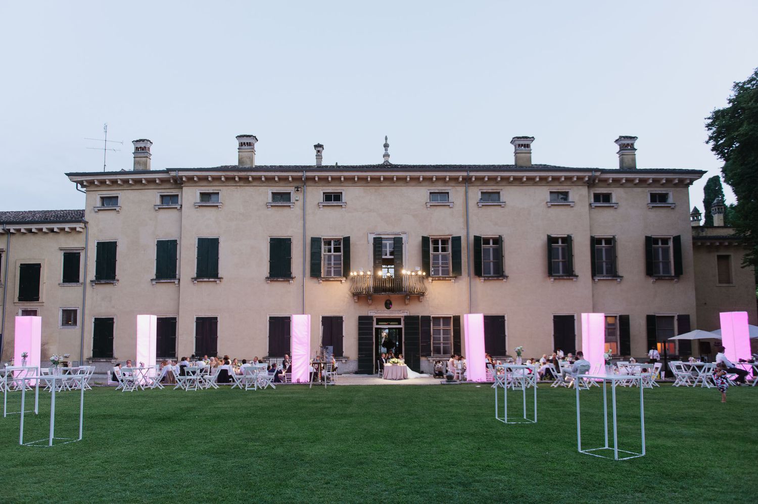 An elegant Italian villa illuminated at dusk with purple lighting and a decorated lawn.