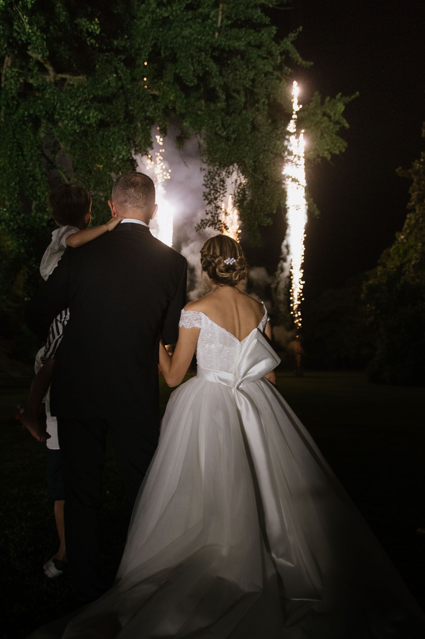 A couple watches fireworks display on their wedding night in a garden setting.