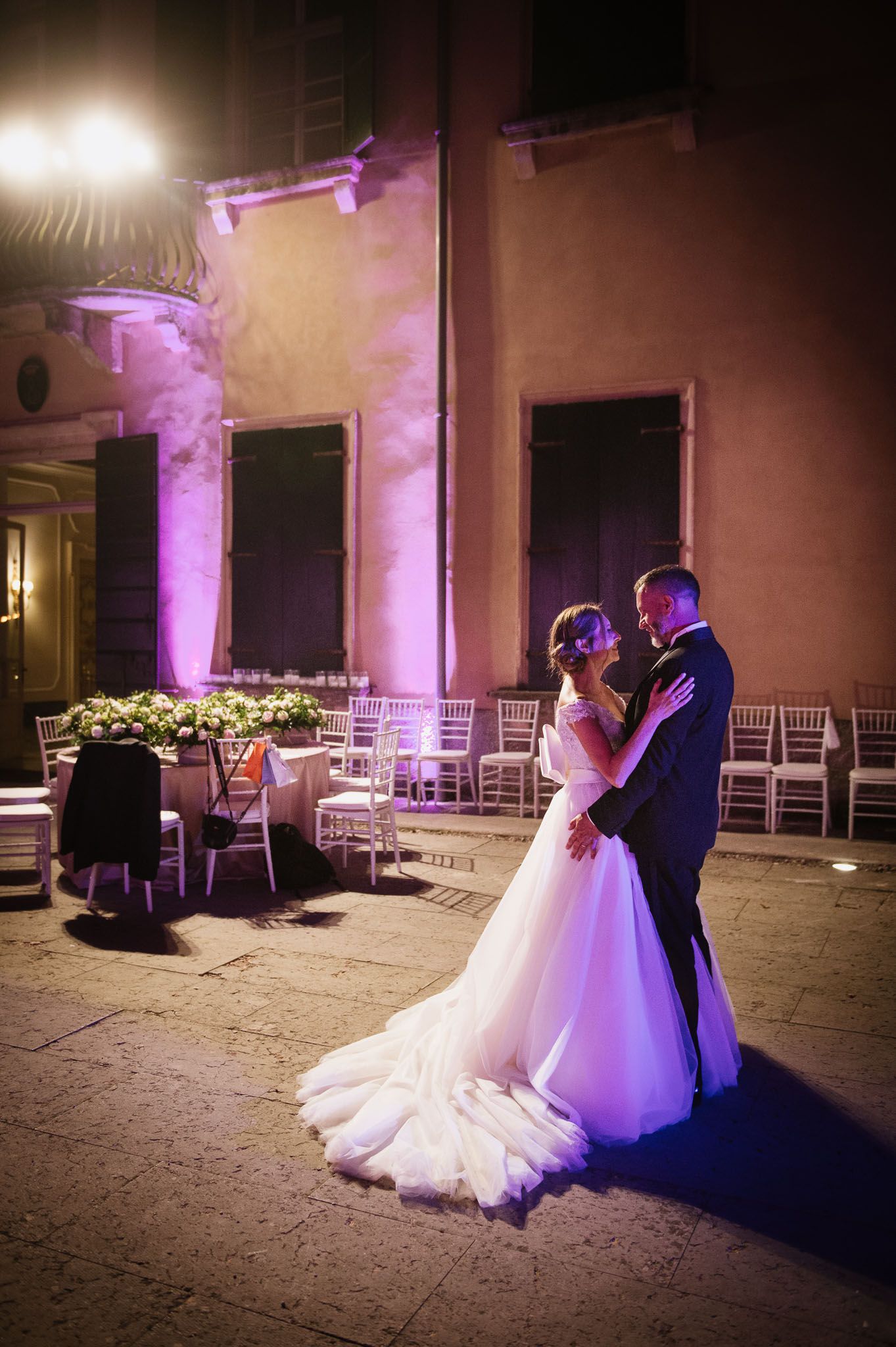 Wedding couple dancing under purple lighting with elegant venue pillars in background.