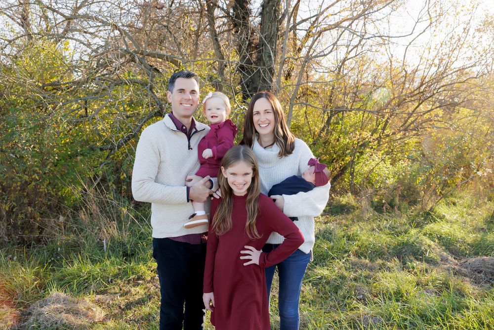 Family of five poses together outdoors in coordinated burgundy and neutral colored outfits.
