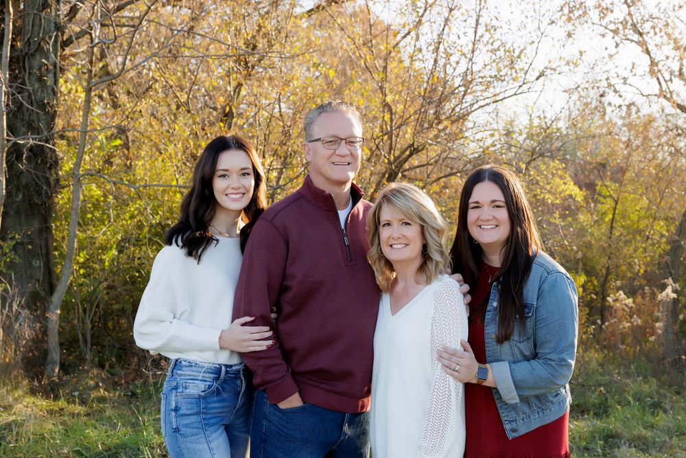 Family group of four poses together in front of autumn foliage.
