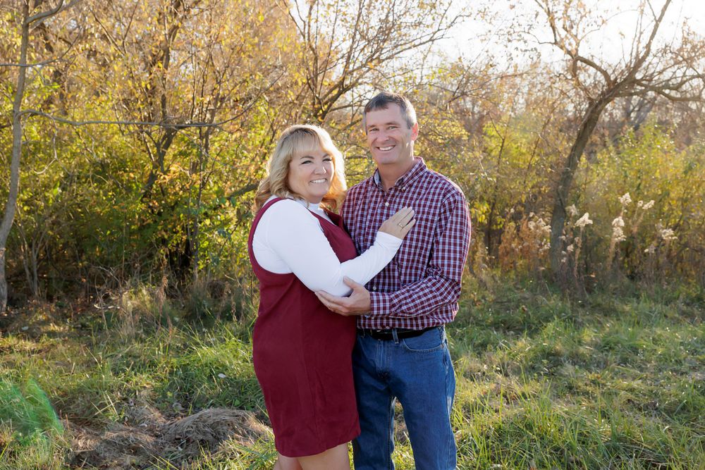Couple poses together outdoors with autumn foliage in the background.