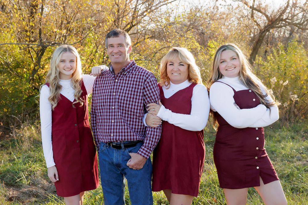 Family of four poses together outdoors wearing coordinated burgundy and white outfits.