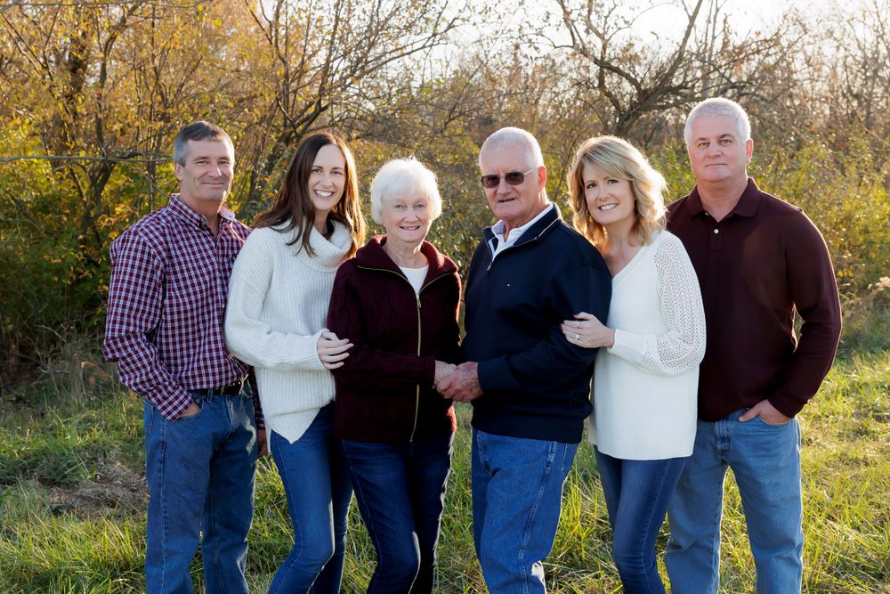 A family group of six poses together for a portrait with autumn trees in the background.