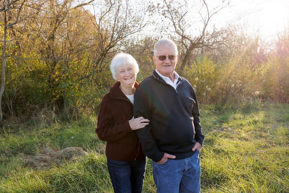 A senior couple embraces while posing for a photo in an autumn outdoor setting.