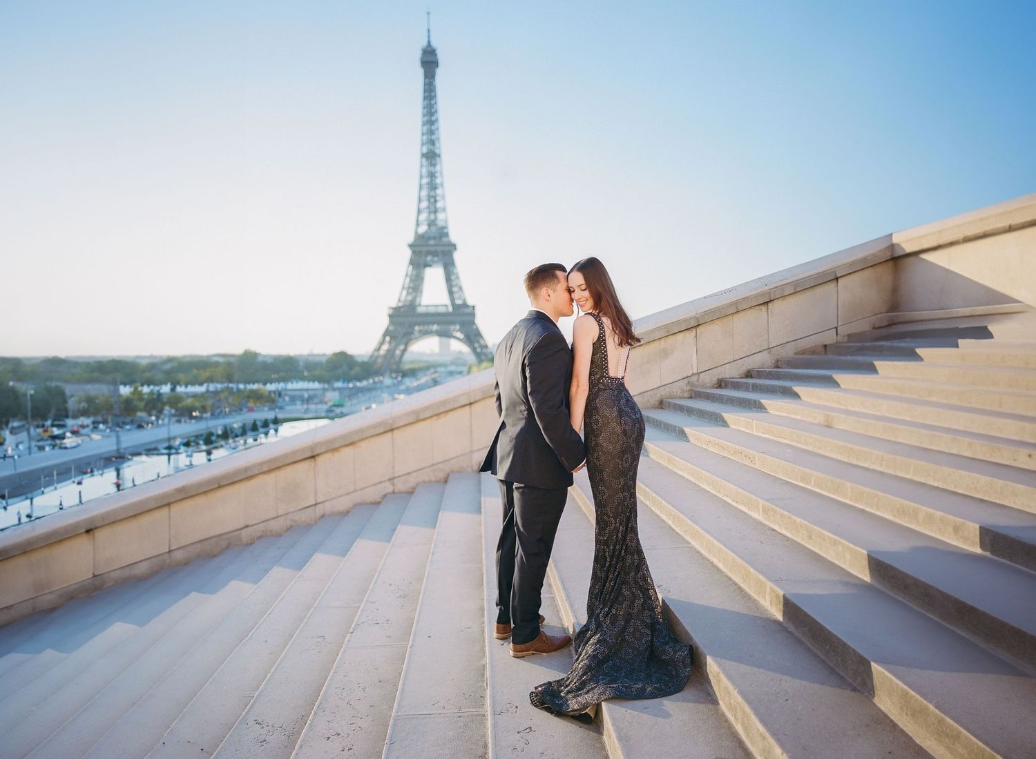 A couple in formal attire stands on steps overlooking the Eiffel Tower in Paris.