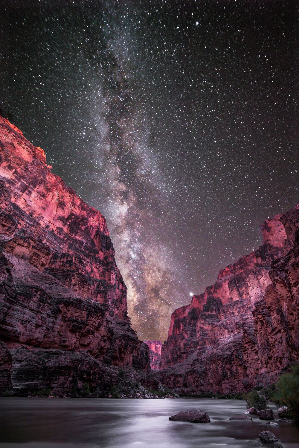 Milky Way galaxy stretches across night sky above red canyon walls.