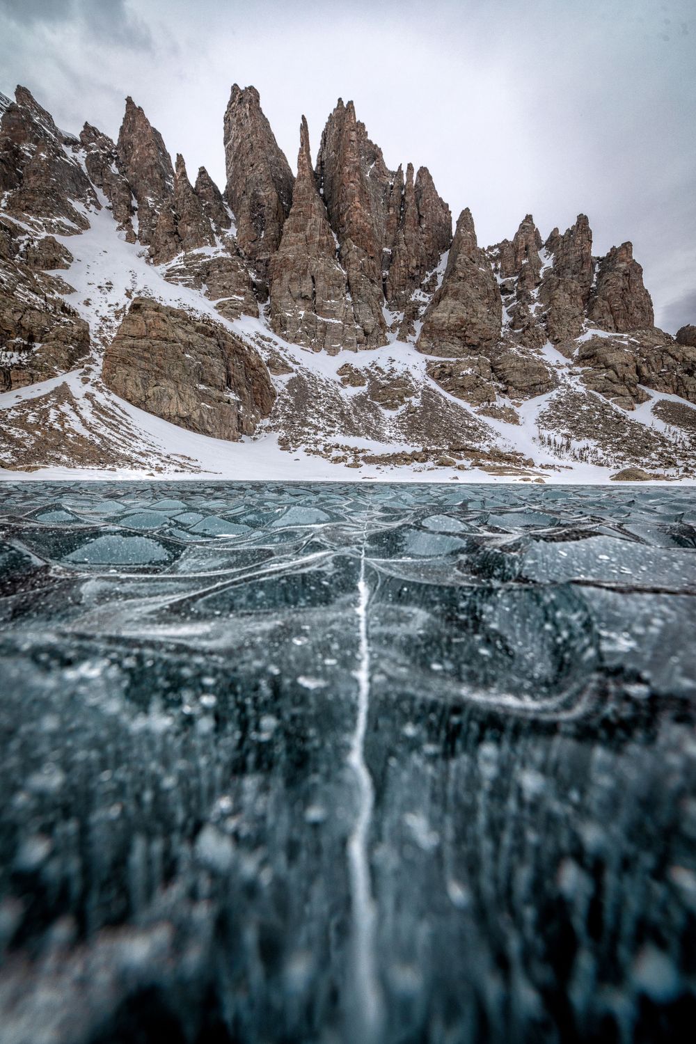 Split-shot photograph showing mountain peaks above and crystal clear ice below the water surface.