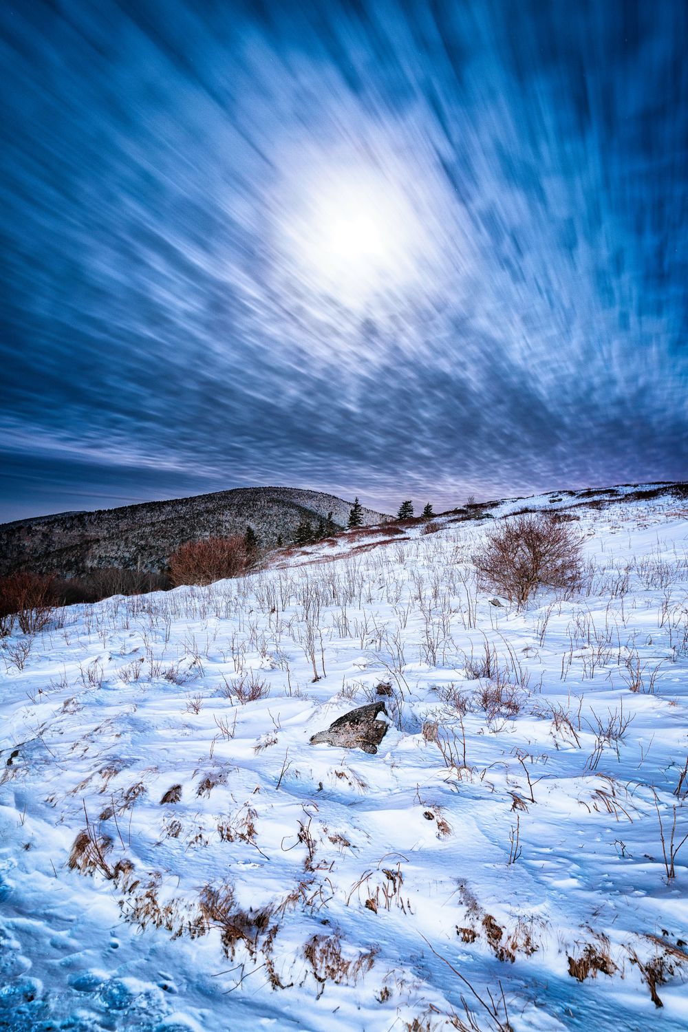 Dramatic winter landscape with snow covered hills and swirling clouds in a vibrant blue sky.