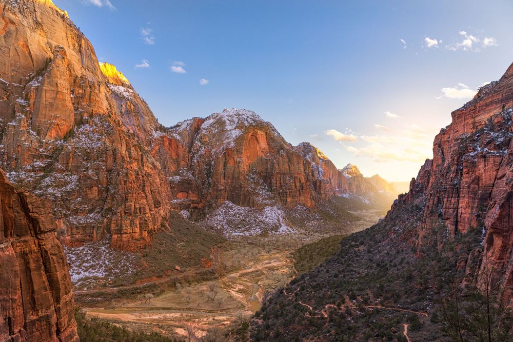 Dramatic red rock canyon walls glow during golden hour with sunlight illuminating the steep cliffs and winding path below.
