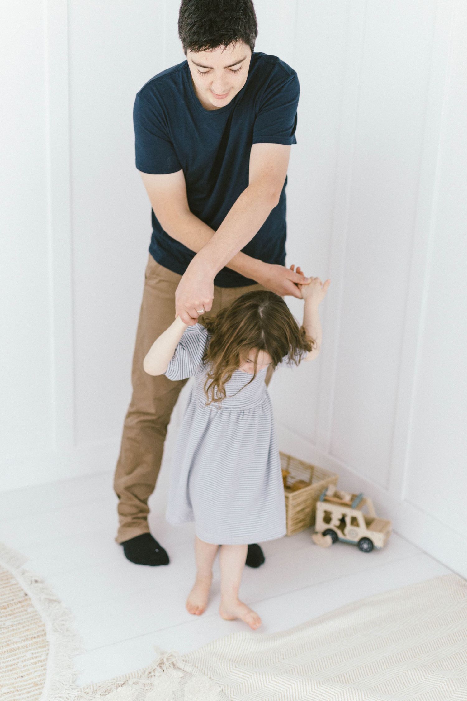 Playful interaction between adult and child in striped dress against white background.