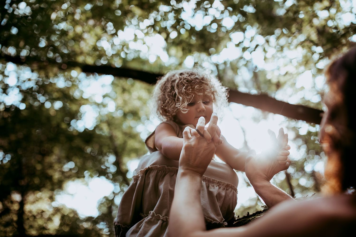 Tender emotional moment between parent and baby outdoors with soft bokeh lighting in nature.