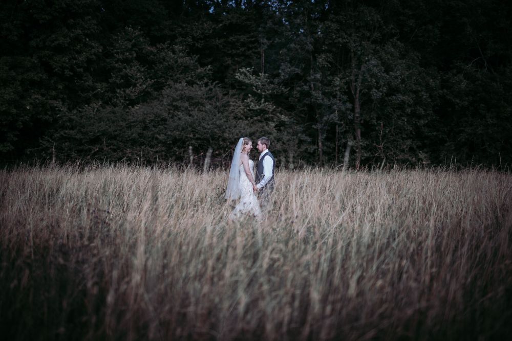 Romantic portrait of a couple standing in tall grass during golden hour.