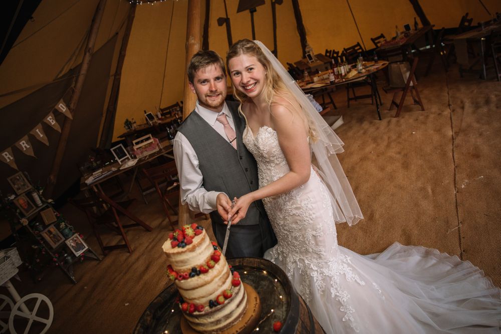 Couple cuts their tiered wedding cake inside a warmly lit reception tent.