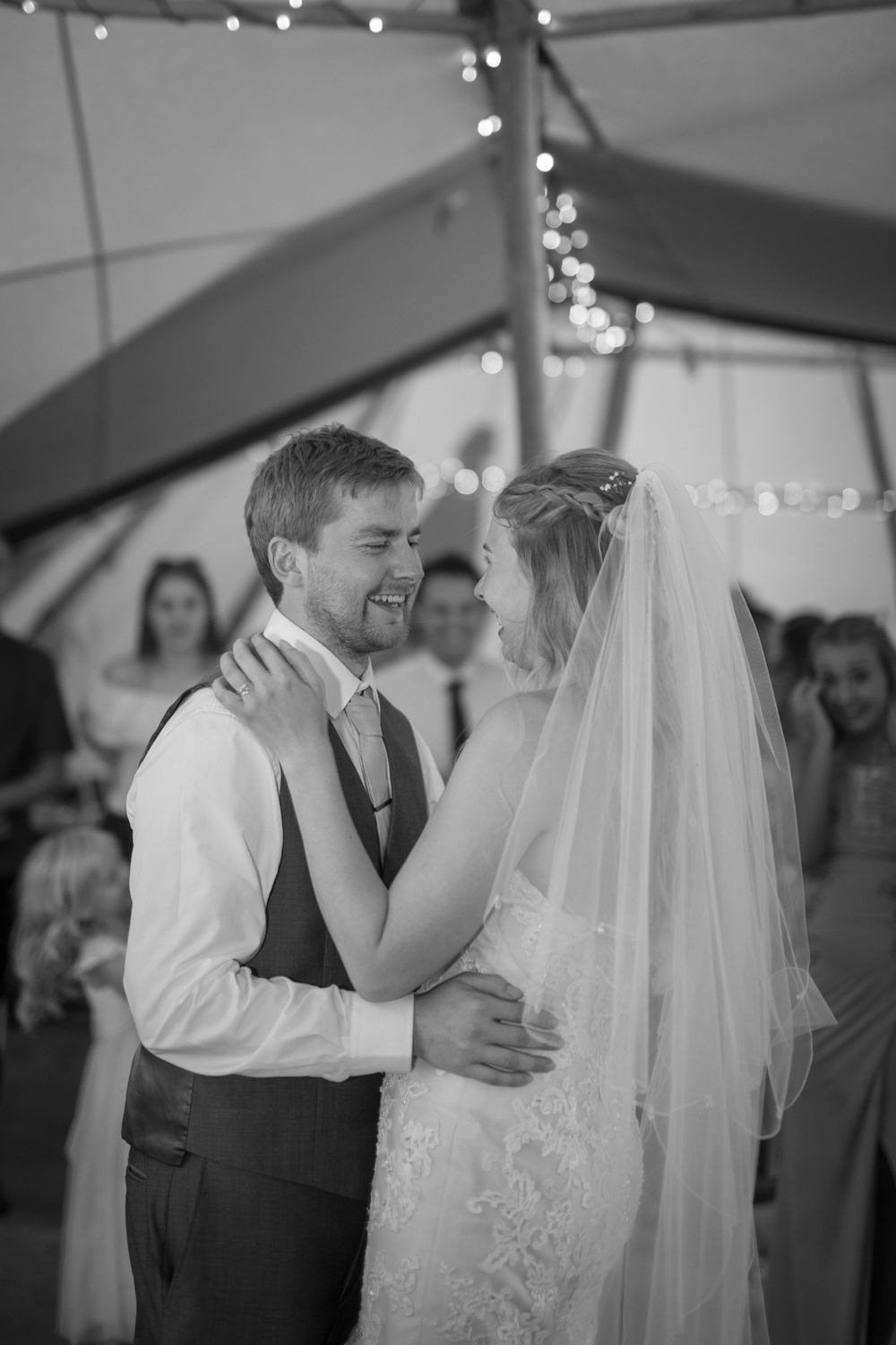 Black and white photo of newlyweds sharing their first dance under twinkle lights in a wedding tent.