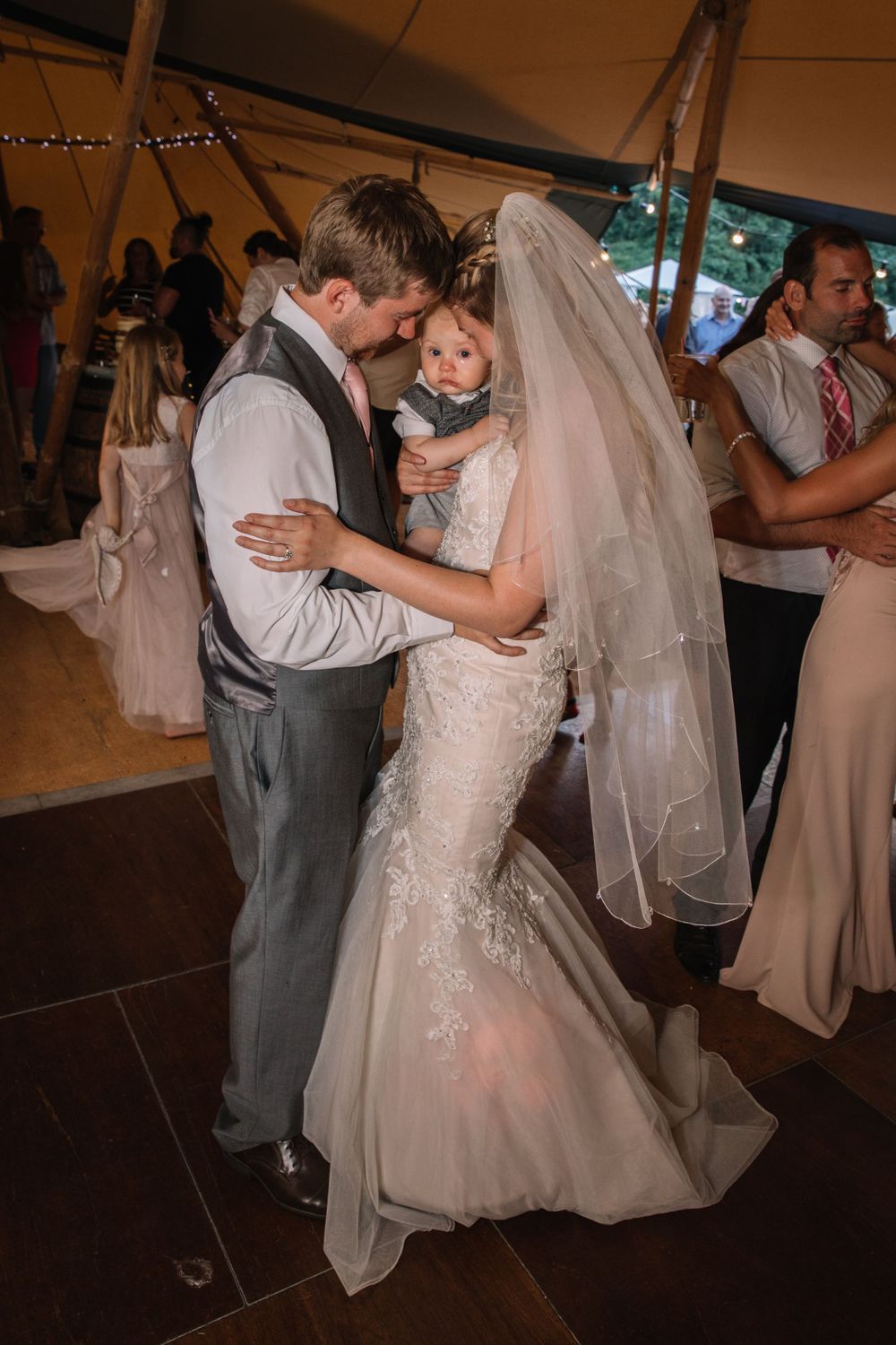 A romantic moment between newlyweds dancing with their baby at their wedding reception in a tent.