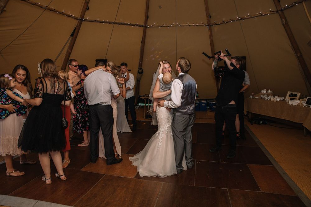 Wedding guests dancing and celebrating in a rustic tent venue with ambient lighting.