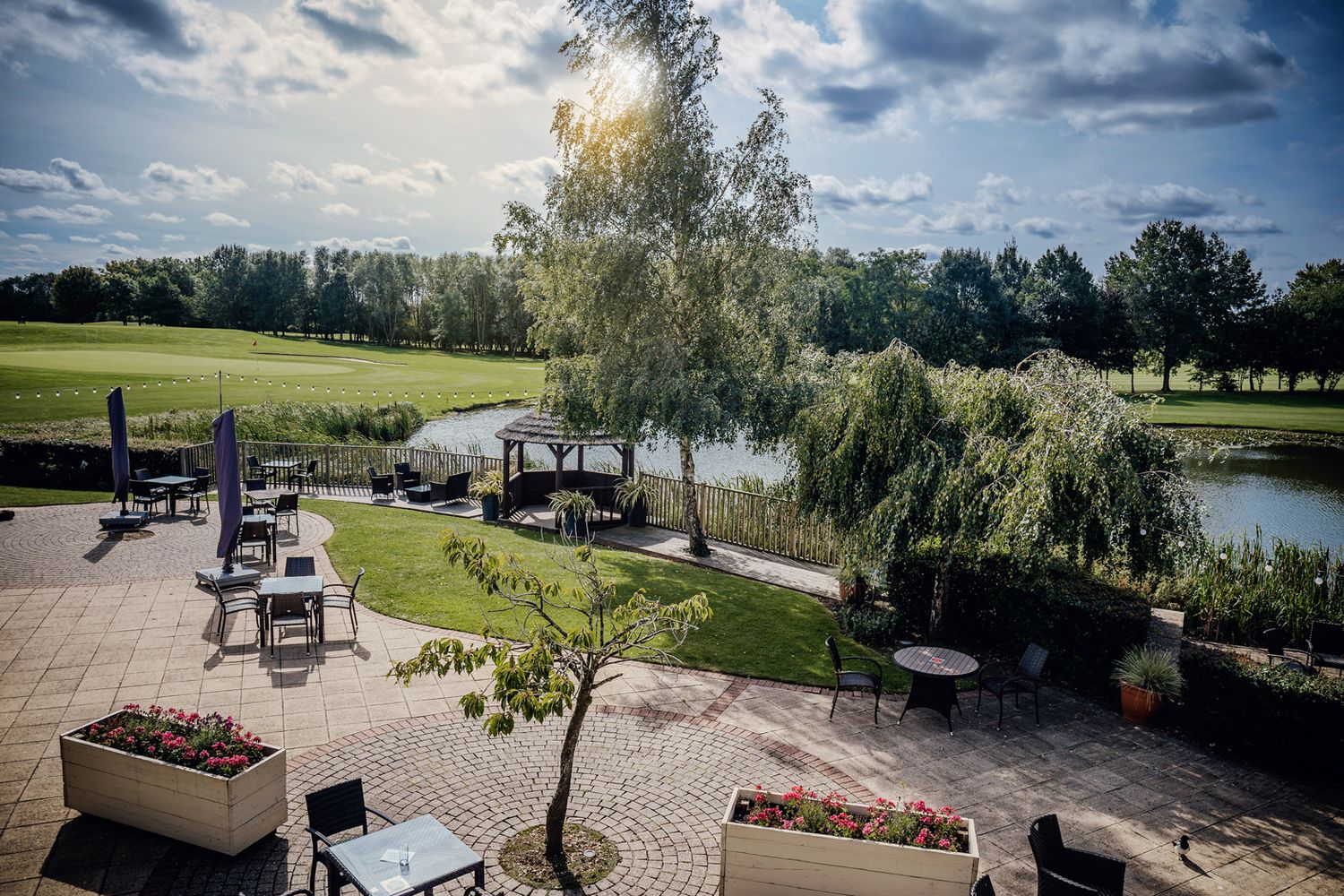Outdoor patio seating area overlooking a pond with willow trees and landscaped grounds.