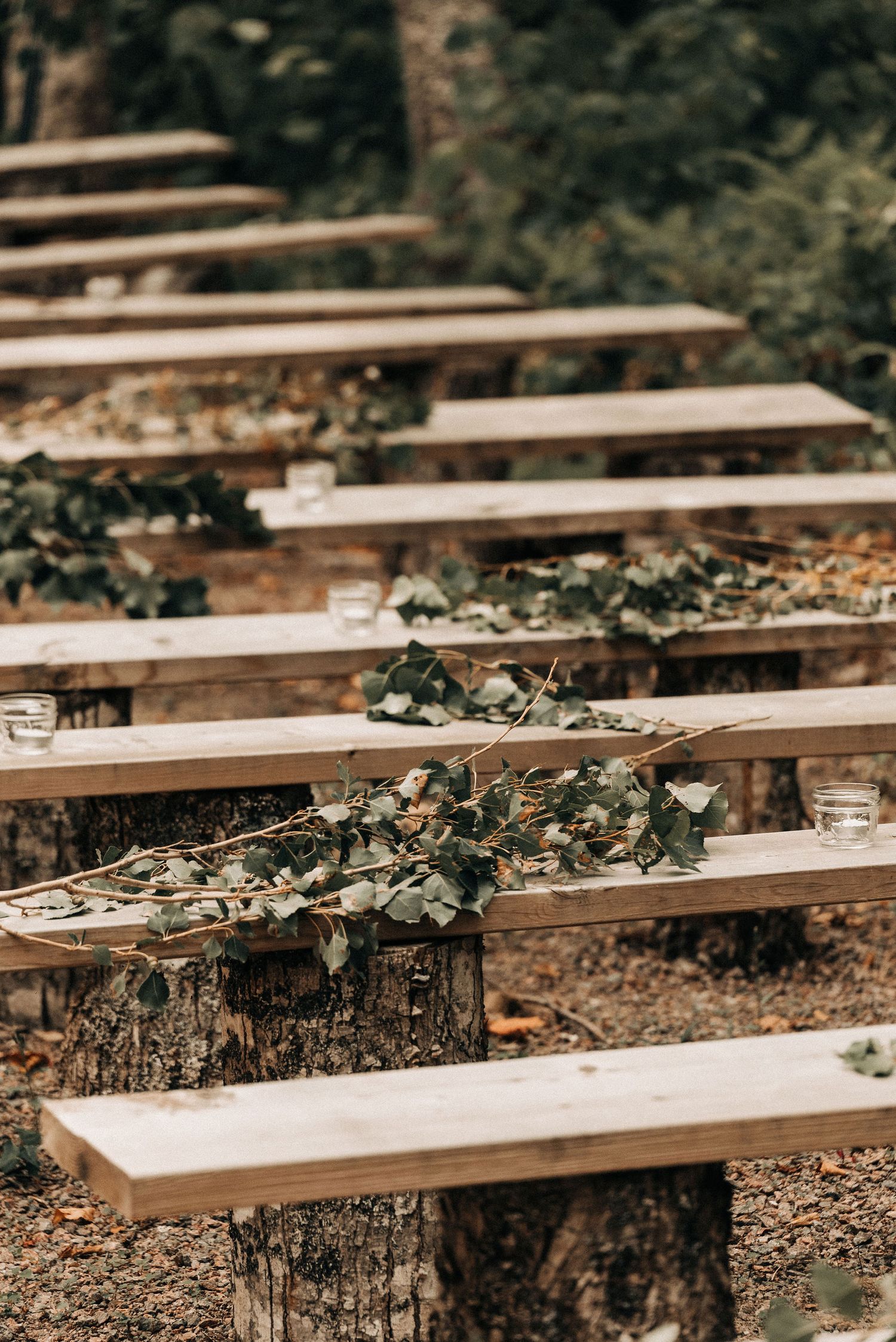 Rustic wooden bench seating decorated with greenery in an outdoor woodland setting.