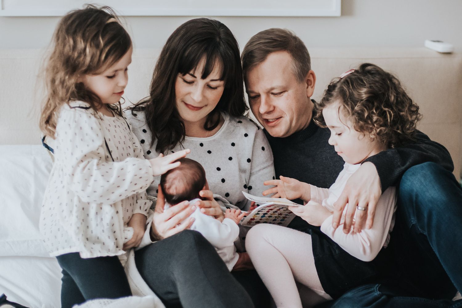 Colour image of a family laying in bed focusing on their newborn daughter and sister.