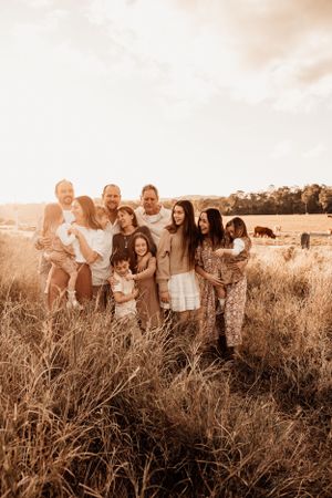 Family gathering in golden sunset field with rustic fence in background.