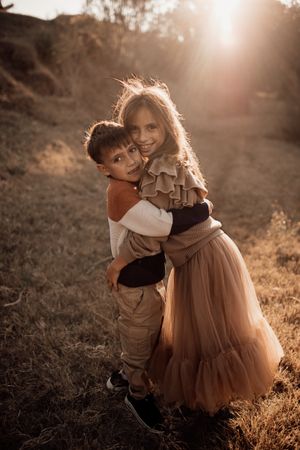 Two young people embrace while posing on a sunlit hillside path.