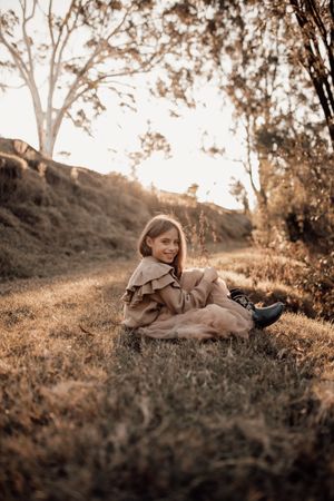 A person in casual attire sits on a grassy hillside during golden hour.