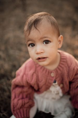 A young child wearing a pink knit sweater sits outdoors.