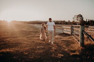 Couple walking along a rustic fence line during golden hour in a pastoral setting.