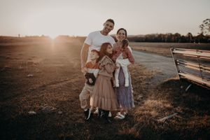 Family portrait at sunset in a rustic field with wooden fence in background.