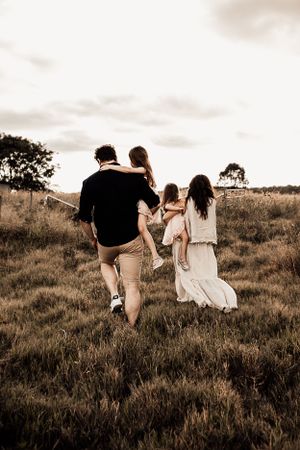 Family walking together through tall grass field at sunset in sepia tones.