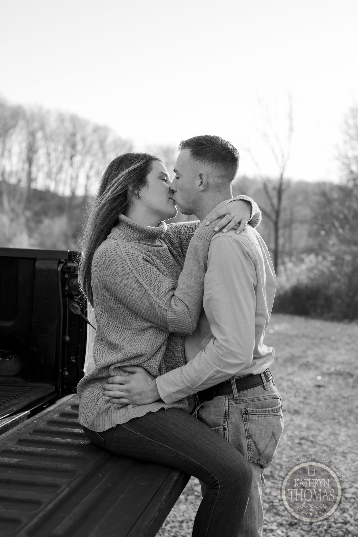 Black and white photograph of couple embracing on pickup truck bed.
