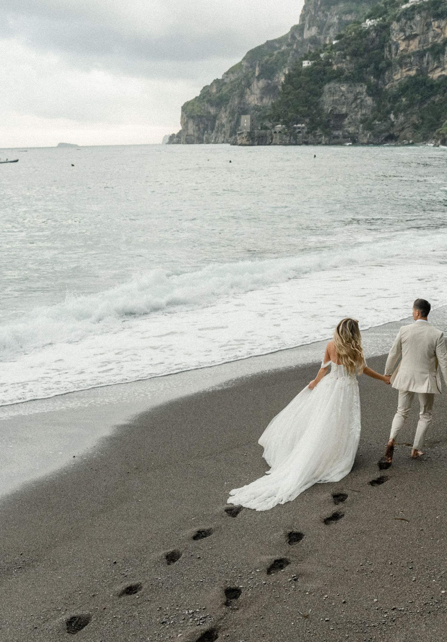 A couple leaves footprints in the dark sand as they walk along a misty Mediterranean beach.
