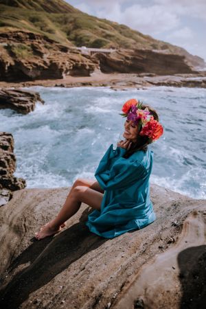 A scenic oceanside portrait with someone wearing a bright blue outfit and floral accessories on rocky cliffs.
