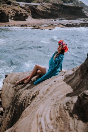 A coastal graduation photoshoot featuring someone in teal regalia posing on dramatic rocky cliffs.